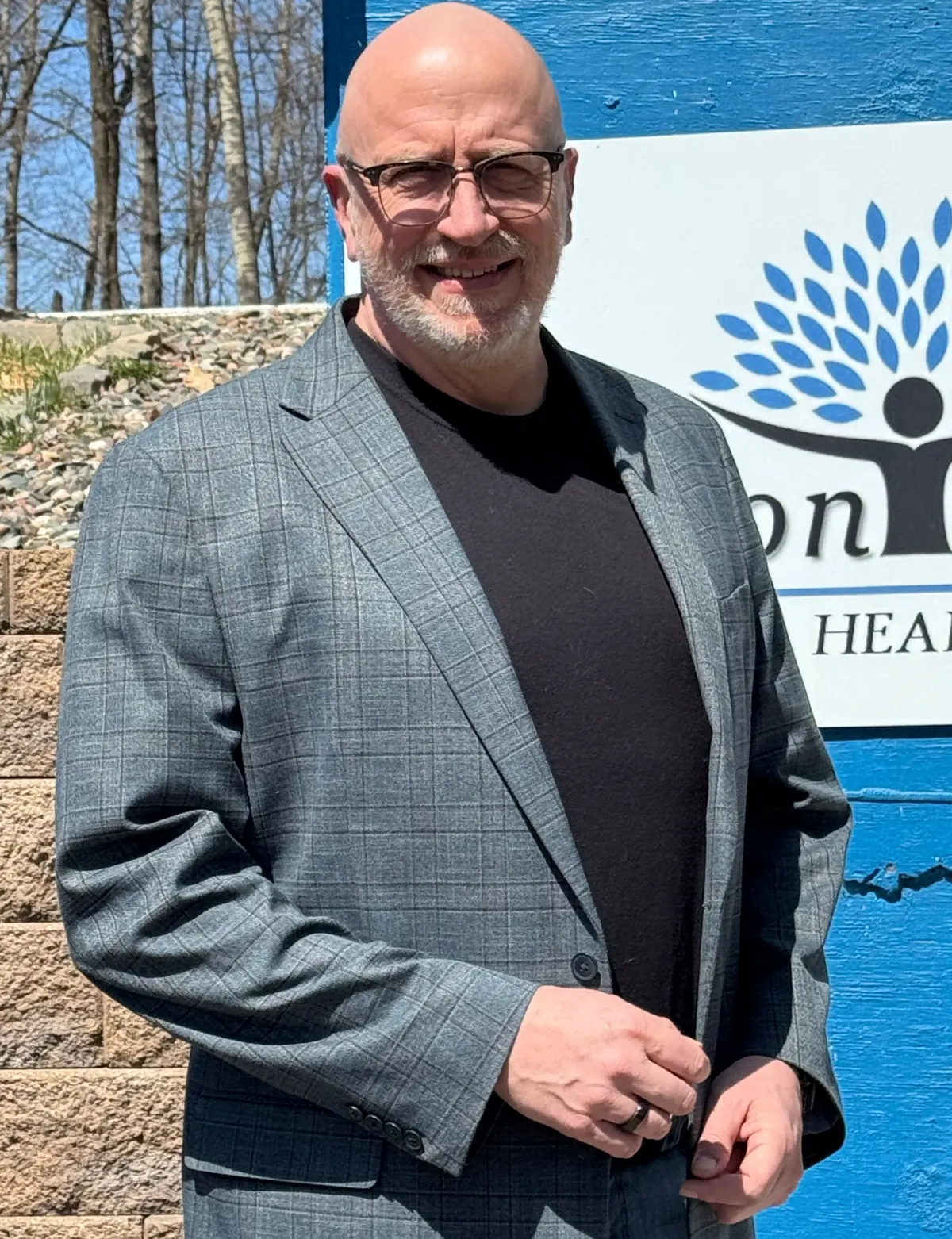 Jeff Evenson in a sport coat, smiling beside the Evenson Holistic sign on the blue office